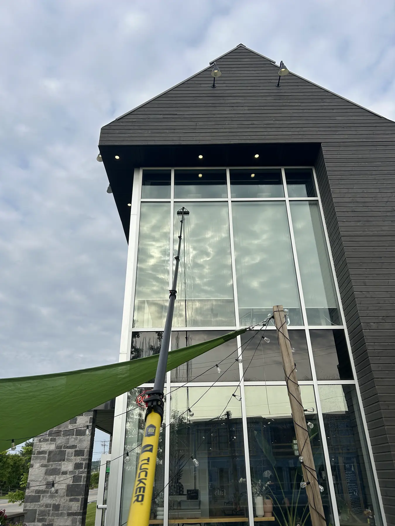 Perche à eau pure en fibre de carbone nettoyant une grande fenêtre à deux étages depuis le sol