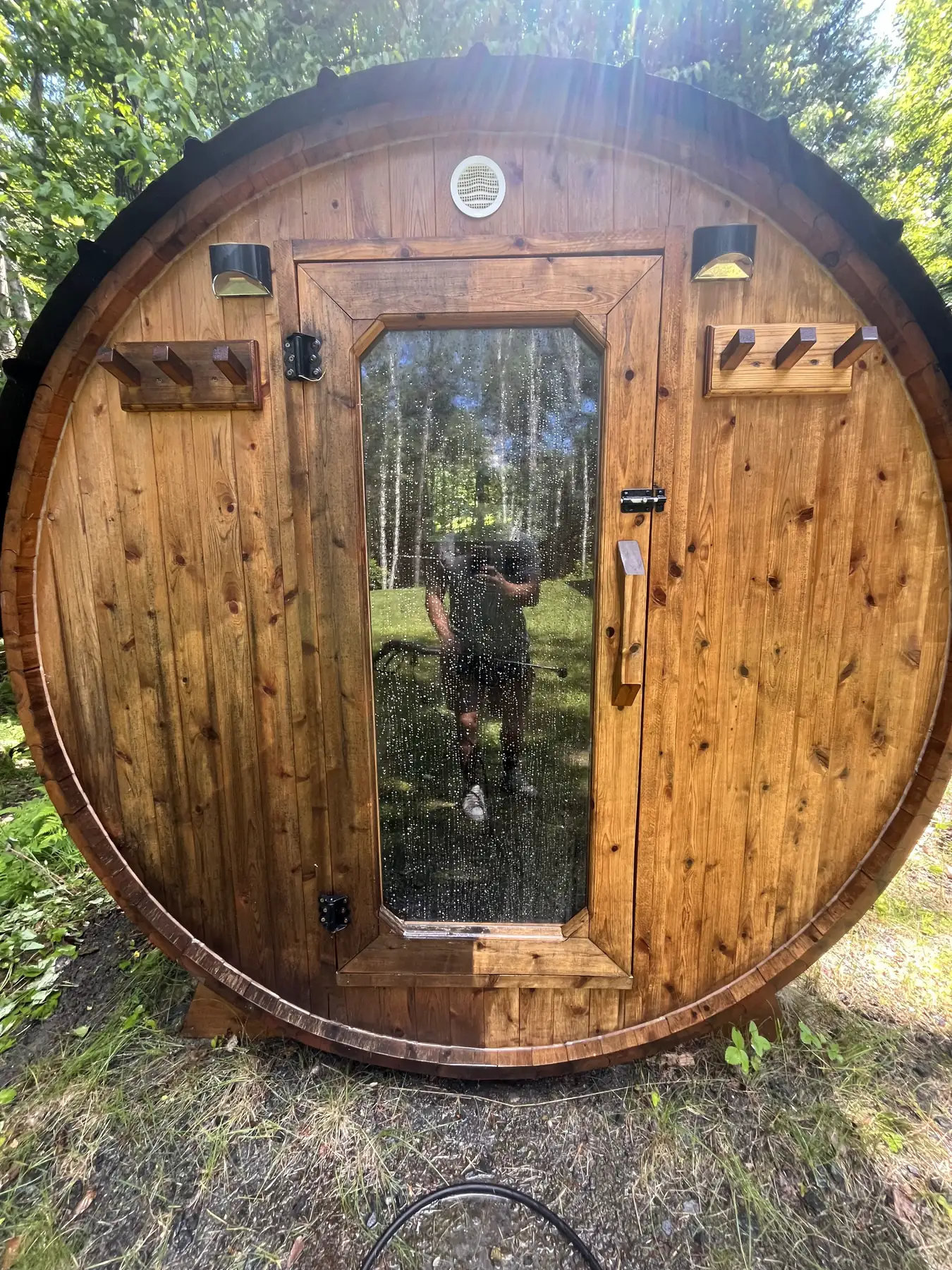 Sauna en baril au milieu des arbres, dont la porte vitrée vient d'être nettoyée