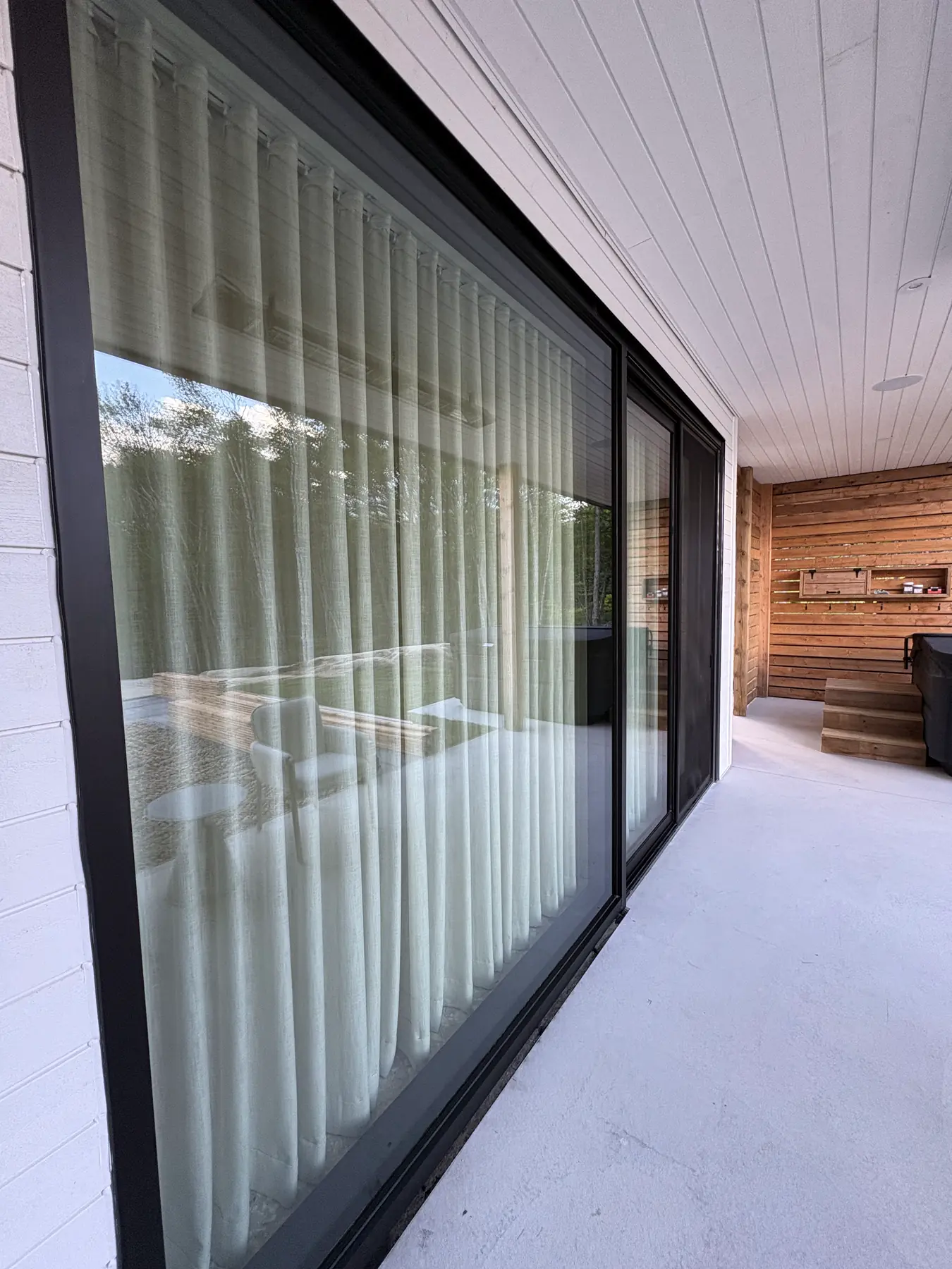 Panneaux vitrés coulissants d'une terrasse couverte donnant sur un sauna